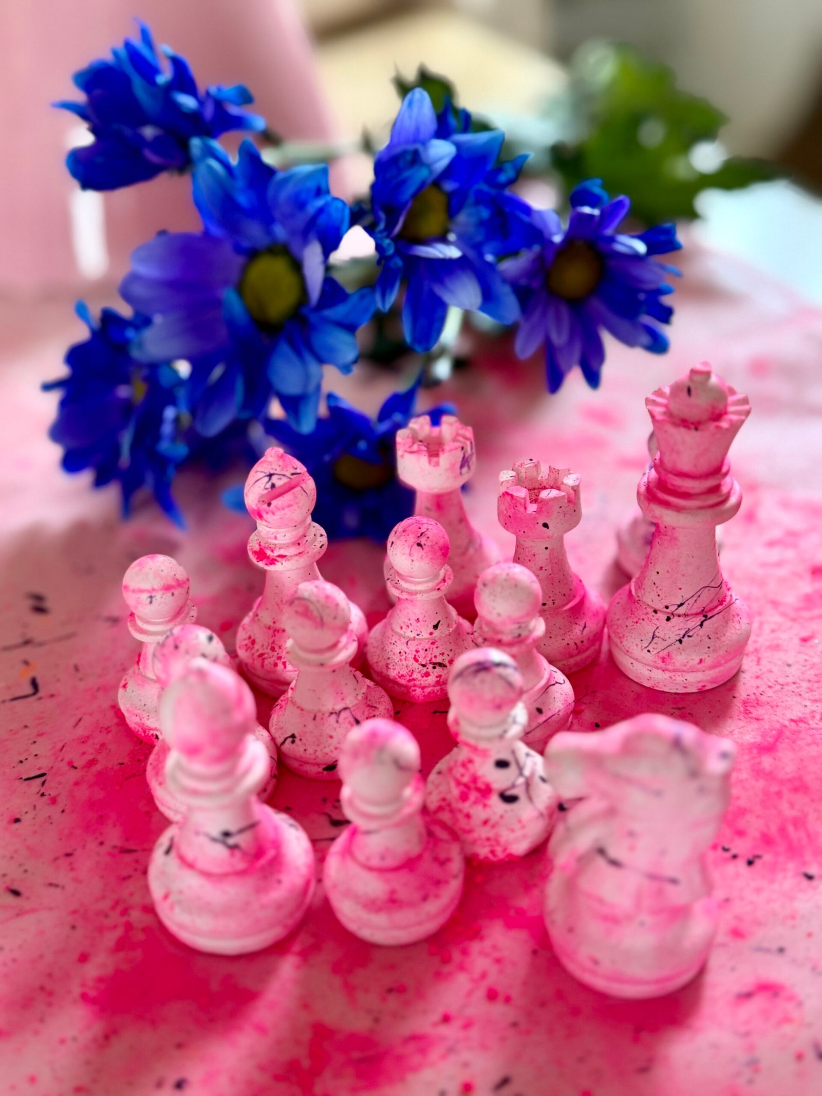 Rosa marmorierte Schachfiguren vor einem Strauß blauer Blumen.